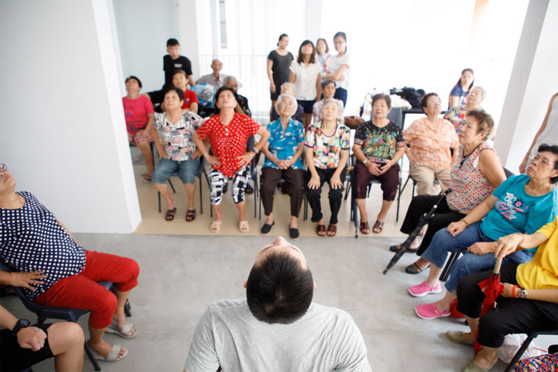 Void deck with a row of seated seniors stretching their backs