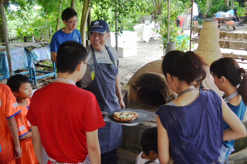 A volunteer instructor demonstrating how to use the earth oven to make pizzas