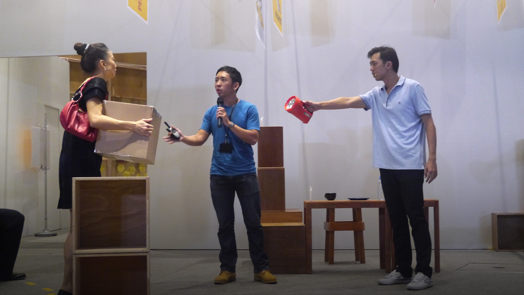 Image taken from IPS Prism (2012) forum theatre where a performer is holding onto a cardboard box and the other torch light with the emcee facilitating the dialogue