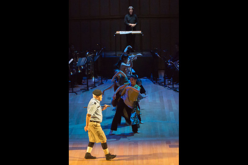 A row of performers dancing behind an actor walking by onstage