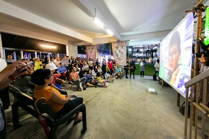 People at a void deck watching a projector screen (Both Sides, Now at Chong Pang)