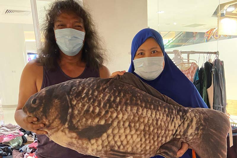 (From left) Sabtu in brown singlet and dark brown shorts, Linda in dark blue tudong and blue floral dress, both holding and posing with a large fish cushion.