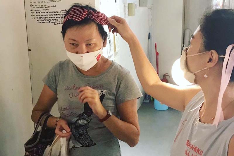 (From left) Legendary Customer Mdm Lim in a grey shirt, wearing a red and white striped headband. Xi Jie extending right hand to help Mdm Lim adjust the headband while holding a few more headbands on her left hand