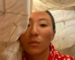 Photo of Salty Xi Jie, wearing a red and white polka dot shirt and appearing to be under a blanket/cloth with the camera taking the photo..