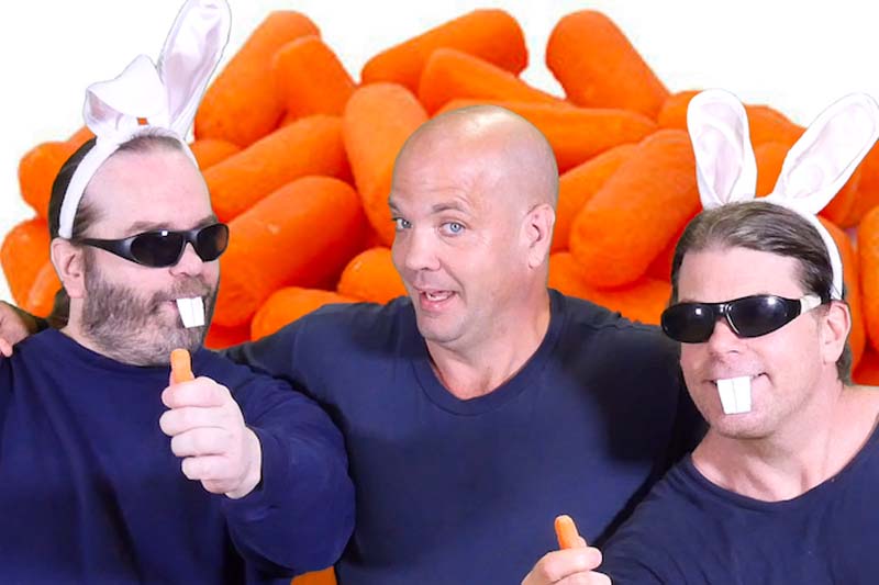 All inmates wearing navy blue t-shirts, posing in front of carrots backdrop. Andrew and Robert wearing bunny ears, black sunglasses, and paper bunny front teeth, each holding mini carrots in their hands.