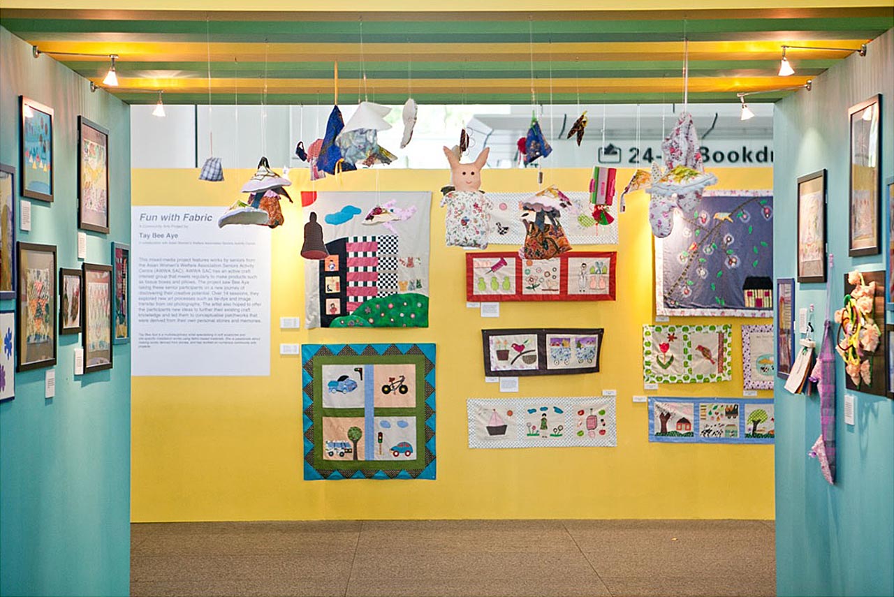 Picture shows the Curator Silverarts Exhibition, yellow walls in the middle with art pieces and green walls at the side. Objects made out of paper hang from the low ceiling.