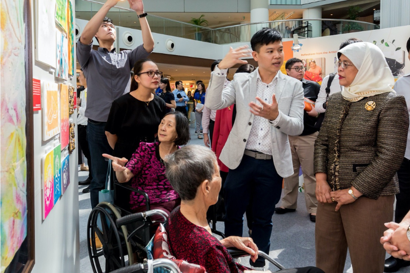 Picture shows Michael Tan explaining an artwork to President of the Republic of Singapore Halimah Yacob during a tour of the Sparks! Art for Wellness Exhibition (2018)