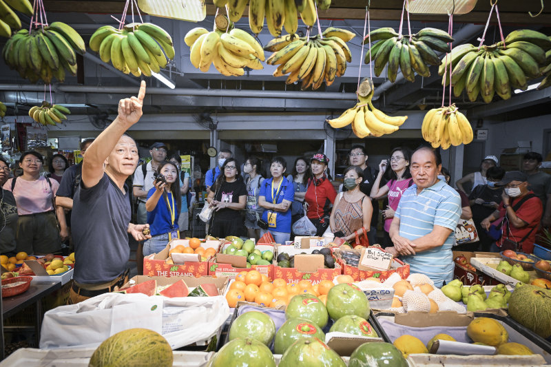 Photo from My Chinatown Festival, organised by My Community, showing a vendor pointing at a bunch of bananas to a group of tour participants