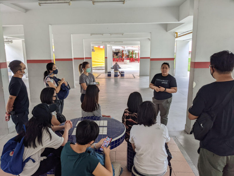 A Community Guide addressing a group of participants during a Resilience Trail at the void deck of a block in Ang Mo Kio