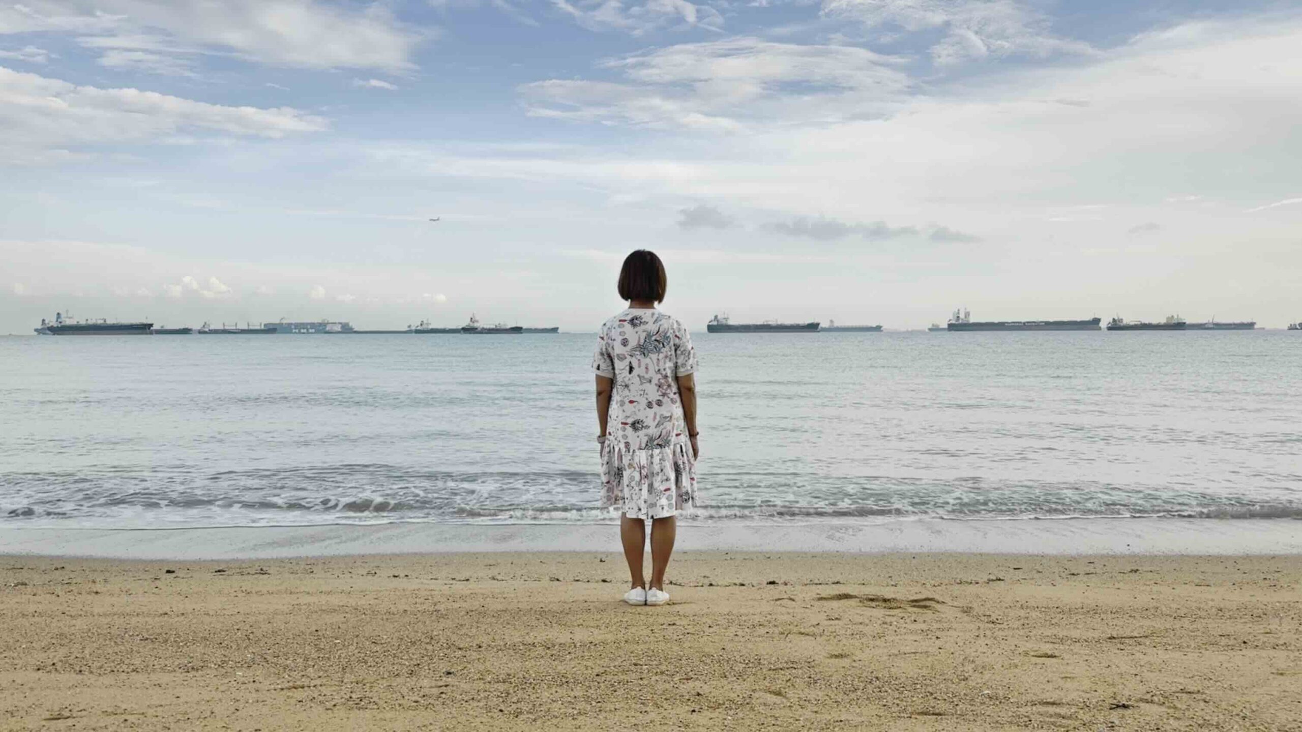 Michelle standing on the shore, facing the sea, reflecting on end-of-life matters.