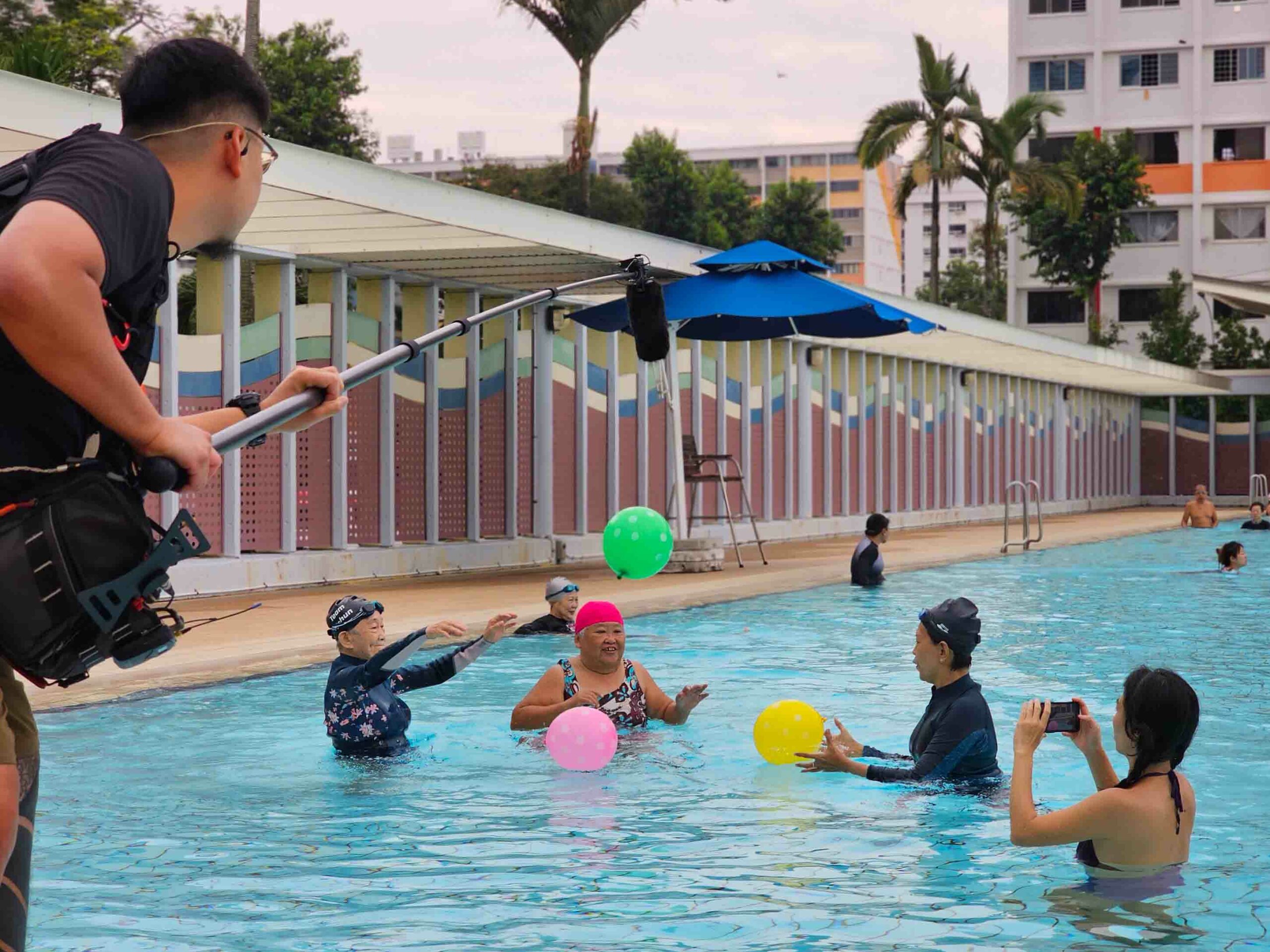 Yim Fong, Michelle, Tong Cheng and Salty in the pool with balloons as a boom operator holds a mic overhead.