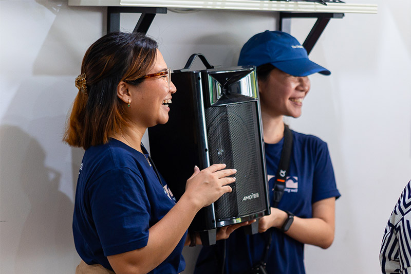 Durrah, accompanied by a volunteer, lifting a portable speaker to shoulder height